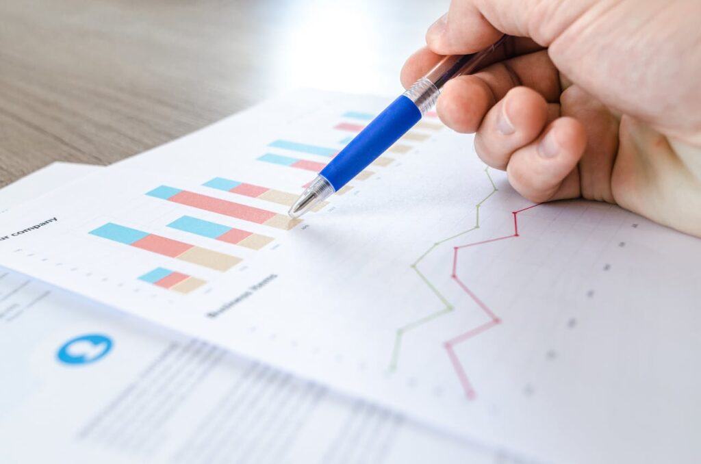 pexels photo 590022 A close-up of a hand with a pen analyzing data on colorful bar and line charts on paper.