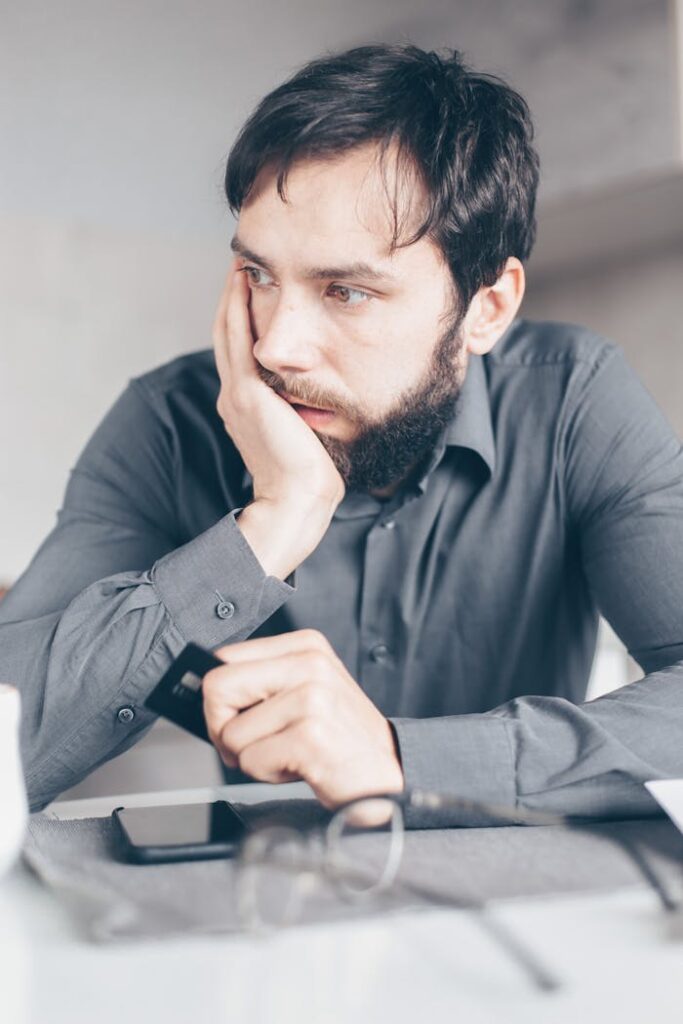 pexels photo 7534778 A worried man in a gray shirt holds a credit card, symbolizing online fraud or financial stress.